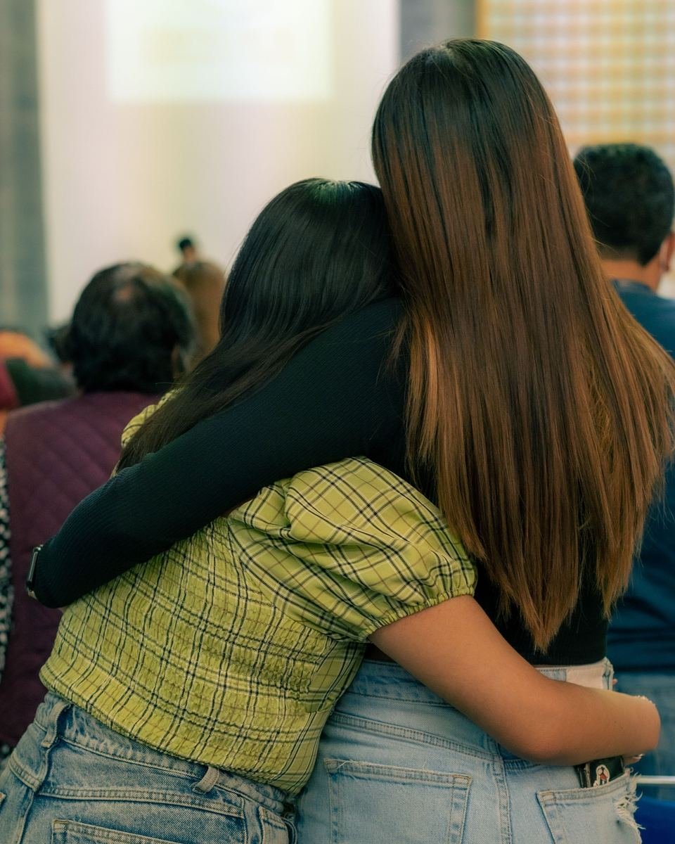Dos mujeres jóvenes, de espaldas, abrazadas por los hombros.